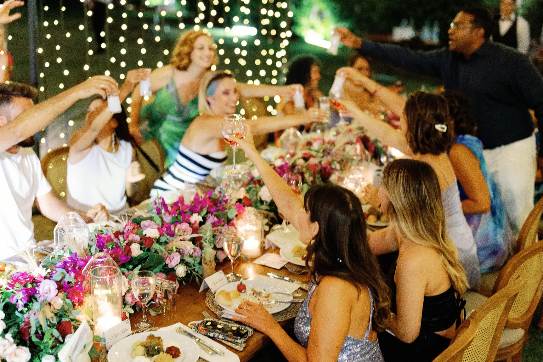 Guests raising a toast at a long garden table under fairy lights on the Riviera